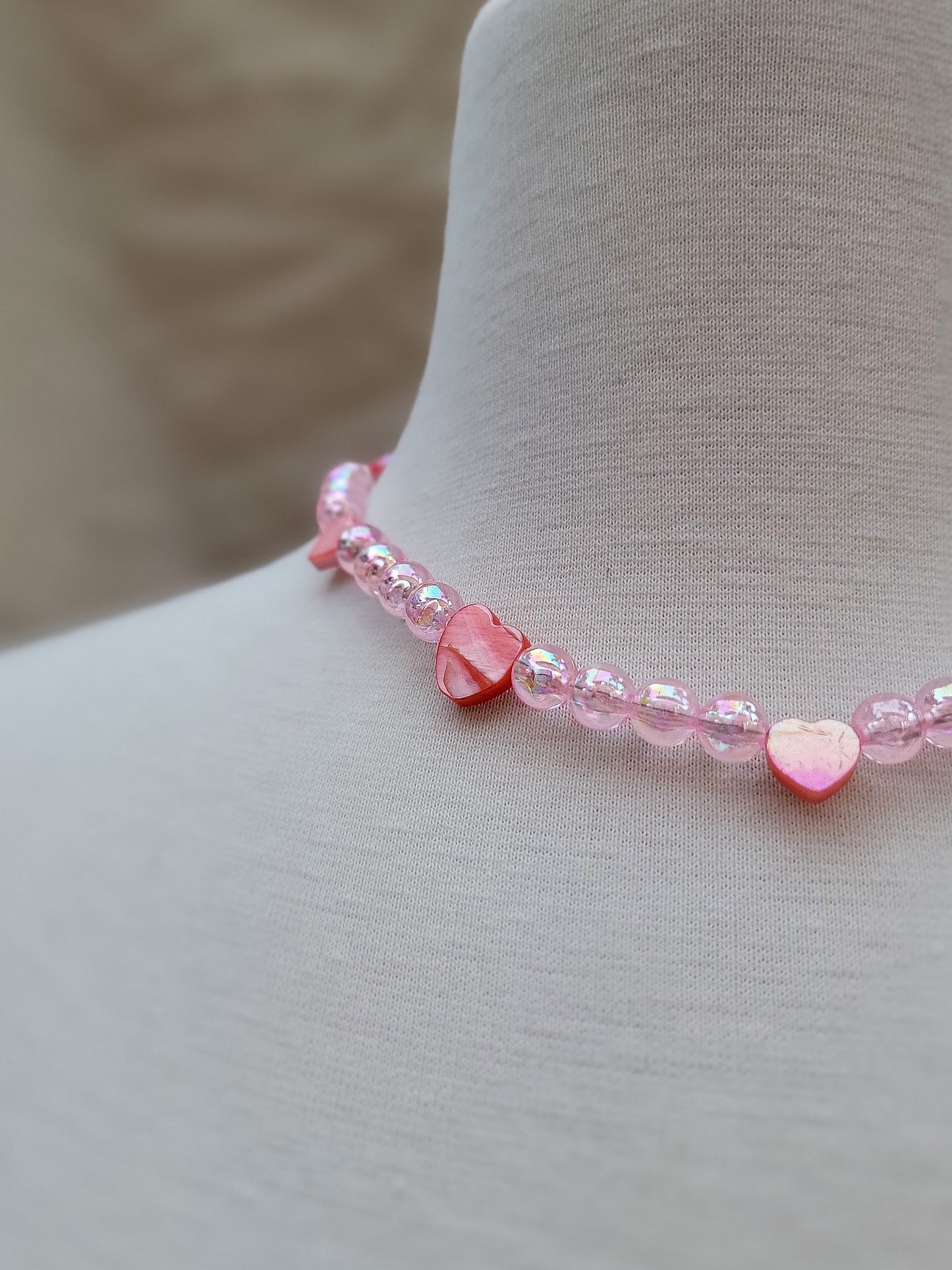 Detalle en primer plano del corazón en nácar rosado tallado a mano y cuentas tornasoladas.