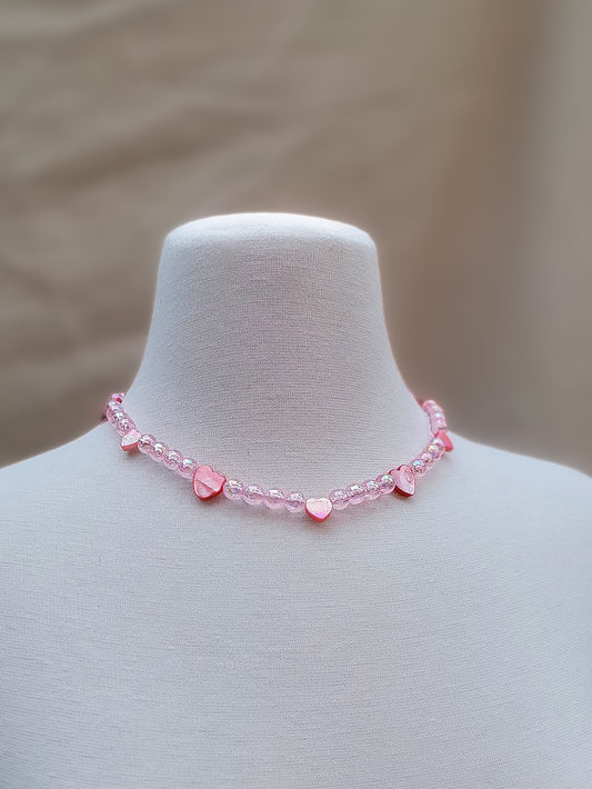 Collar artesanal rosado con corazones de nácar y cuentas acrílicas iridiscentes sobre maniquí blanco – estilo Y2K coquette.