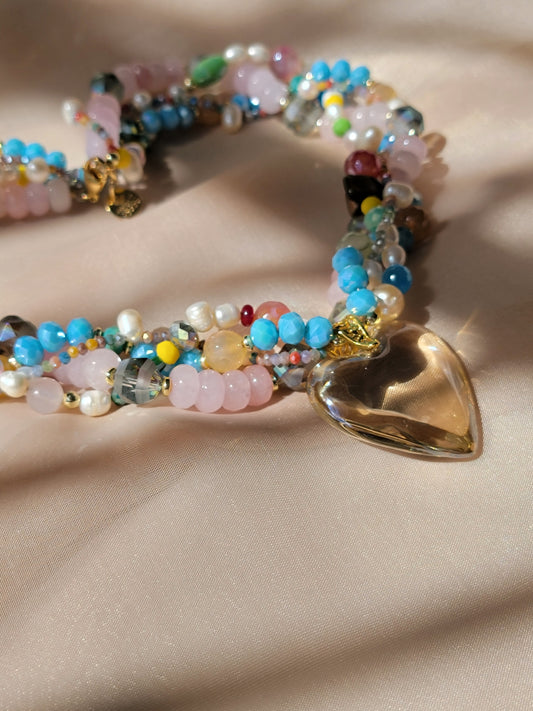 Collar multicolor con corazón transparente – vista frontal sobre tela dorada